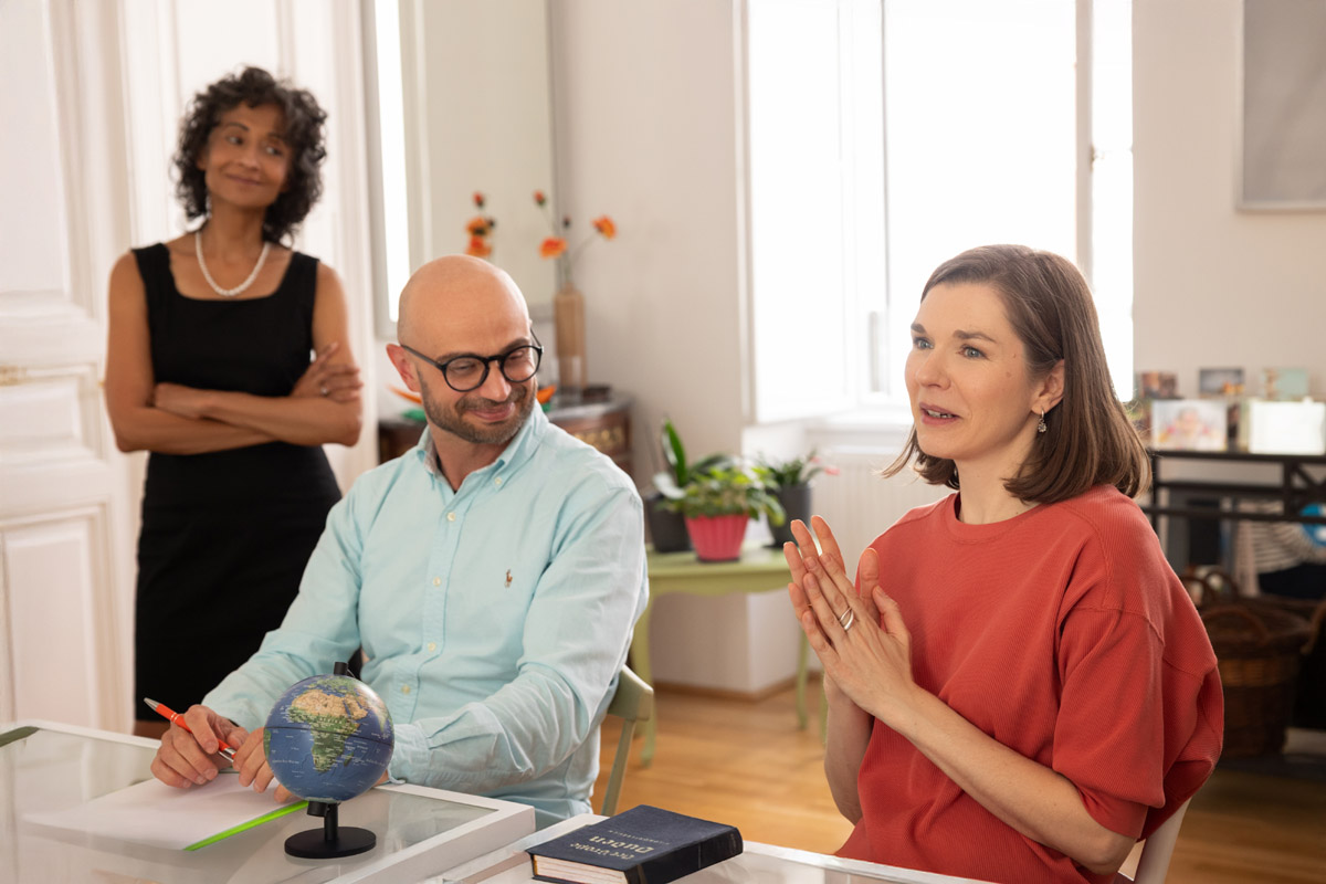 A workshop participant talking next to one who is smiling, with Michèle Cooke standing in the background.